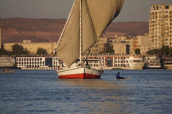 Felucca on the Nile in Aswan with buildings and desert hills in the background.