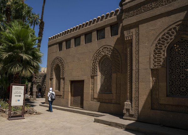 The carved stone facade of Manial Palace's Hunting Museum building in Cairo, with palm trees in the courtyard.