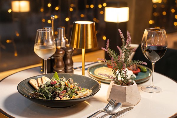 An elegant restaurant table set for two with wine glasses, plated dishes, and warm ambient lighting.