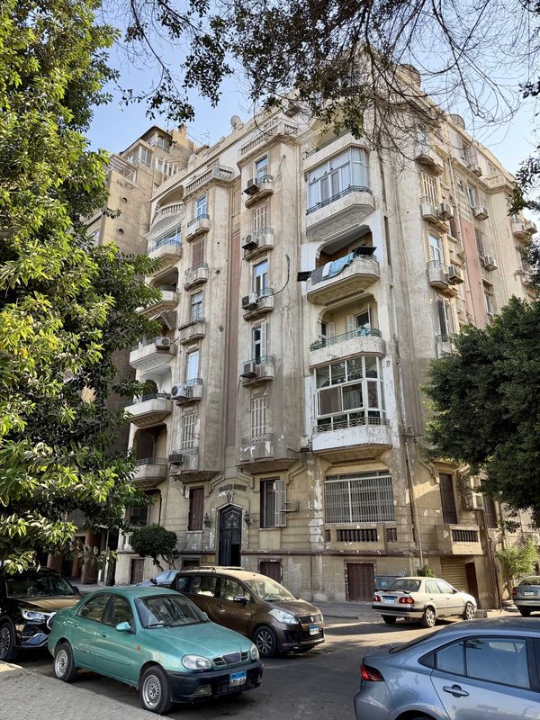 A tree-lined residential street in Zamalek, Cairo, with elegant balconied apartment buildings.