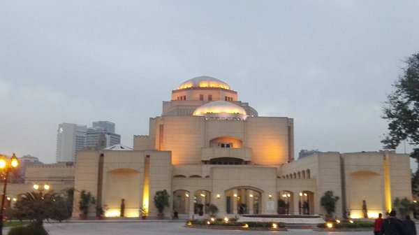 Evening view of the illuminated Cairo Opera House, with cloudy sky and distinctive architectural details.