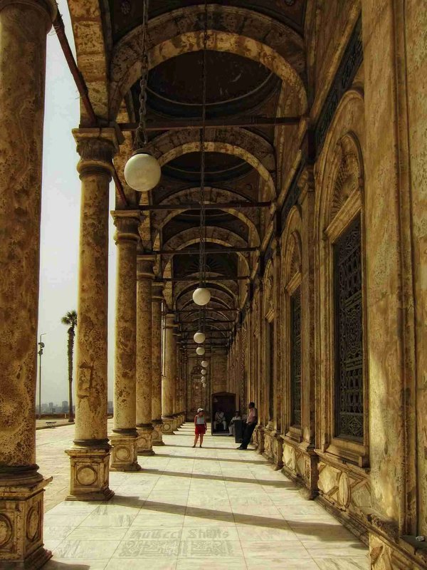 Historic colonnade of a mosque in Cairo with marble arches and columns, illuminated by sunlight.