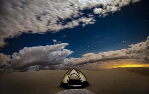 Illuminated tent in the desert under a starry sky with dramatic clouds, near Cairo.