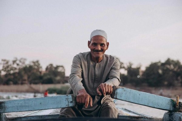 Man on a wooden felucca on the Nile at sunset, with trees in the background.