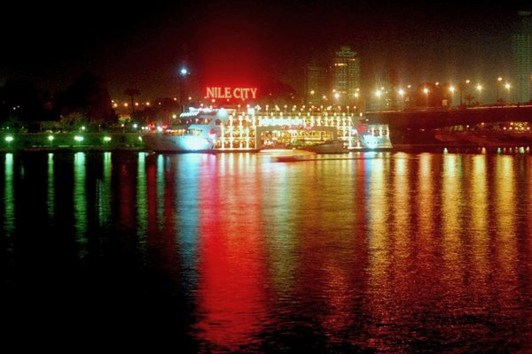 Illuminated Nile boats moored along the Cairo riverbank at night, their lights reflecting on the water.
