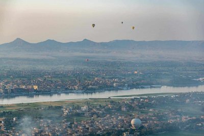 Panoramic view of Luxor with the Nile, hot air balloons, and surrounding landscape at sunset.