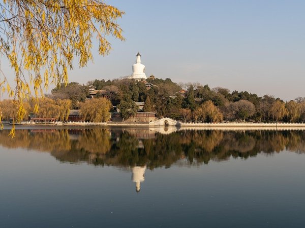Vista del Dagoba Bianco e del lago nel Parco Beihai a Pechino, con riflessi sull'acqua e alberi autunnali.