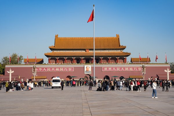 Piazza Tiananmen a Pechino con la Porta Tiananmen, bandiere rosse e folla di visitatori in una giornata di sole.