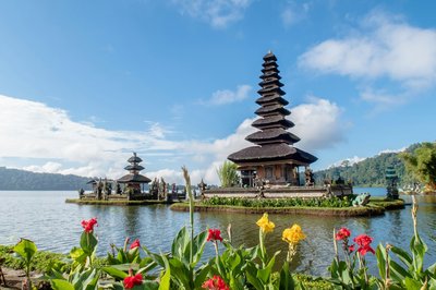 Ulun Danu Beratan Temple in Bali with colorful flowers in the foreground and a blue sky in the background.