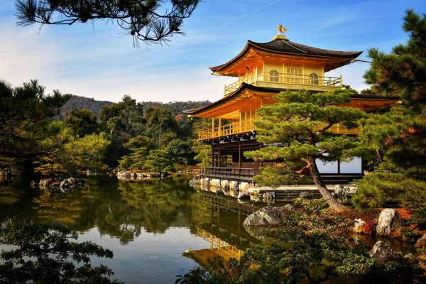 View of Kinkaku-ji, the Golden Pavilion in Kyoto, surrounded by trees and reflected in a serene pond.