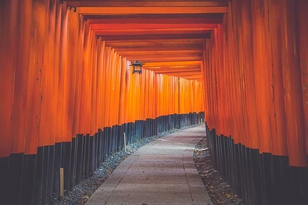 Corridor of red torii gates at Fushimi Inari-taisha Shrine in Kyoto, Japan, with a curved path and a hanging lantern.