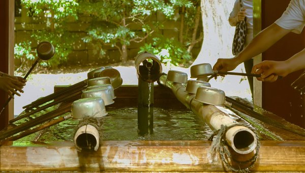 Traditional Japanese purification fountain with metal ladles, surrounded by greenery in Kyoto.