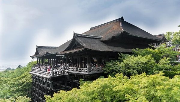 View of Kiyomizu-dera Temple in Kyoto surrounded by green trees under a partly cloudy sky.