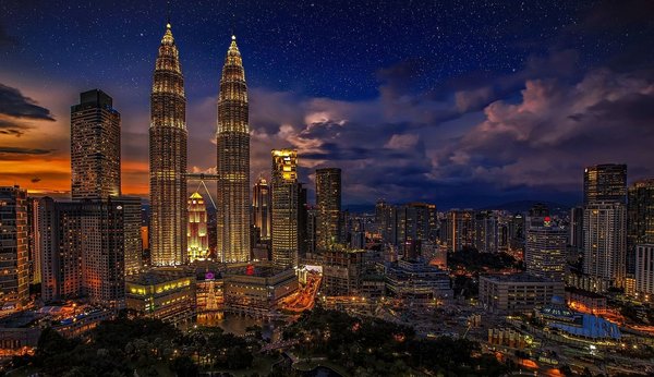 Night view of the illuminated Petronas Towers in Kuala Lumpur with a starry sky in the background.
