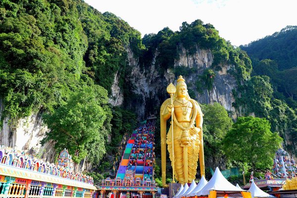 Golden Lord Murugan statue and colorful staircase leading to Batu Caves, surrounded by lush greenery.
