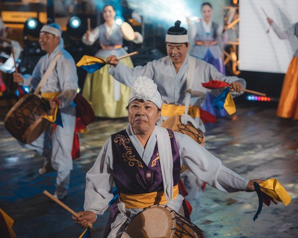 Percussionisti coreani tradizionali in hanbok si esibiscono in una vivace danza pungmul con nastri colorati sul palco.