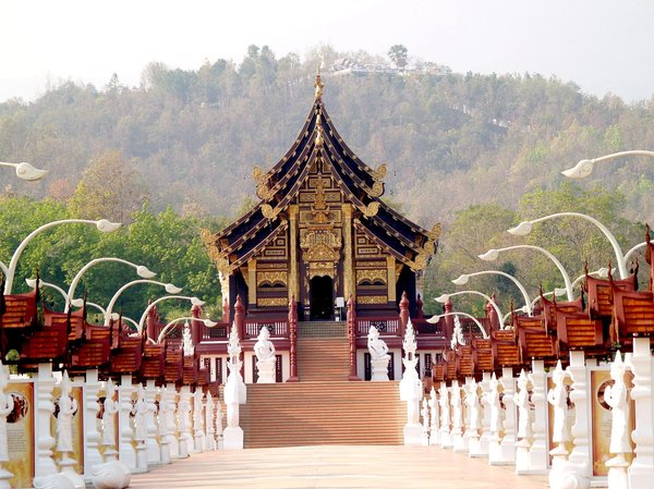 Traditional temple with golden decorations and ornate walkway in Chiang Mai, surrounded by trees and hills.