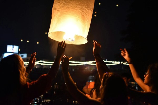 Illuminated lantern rising into the sky during the Lantern Festival in Chiang Mai, with people releasing it.