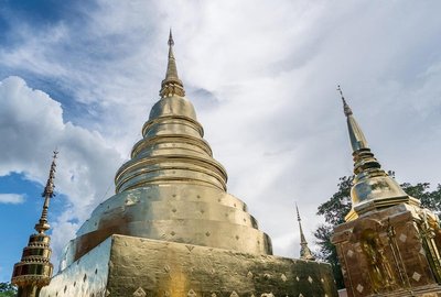 View of a large golden stupa in Chiang Mai with blue sky and clouds in the background.