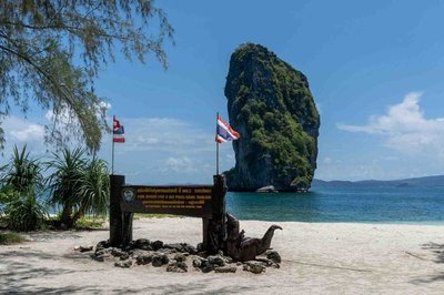 Panoramic view of Krabi with a sandy beach, limestone formation, and a national park sign.