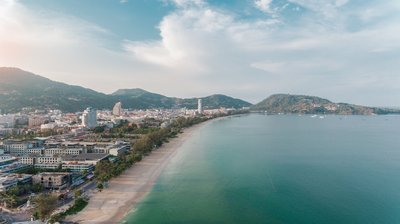 Panoramic view of Patong with sunset, palm trees, pool, and sea in the background.