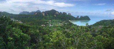 Panoramic view of Phi Phi with limestone cliffs, lush vegetation, and turquoise sea under a partly cloudy sky.