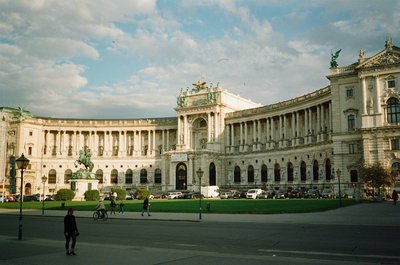 Panoramic view of Hofburg Palace in Vienna with a partly cloudy sky and people strolling.