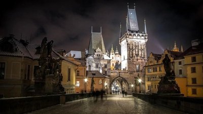 Night view of Charles Bridge in Prague with illuminated Gothic towers and historic statues.