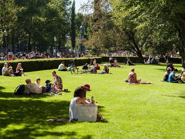 Persone che si rilassano nel Parco Esplanadi a Helsinki in una giornata di sole, con una statua visibile sullo sfondo.