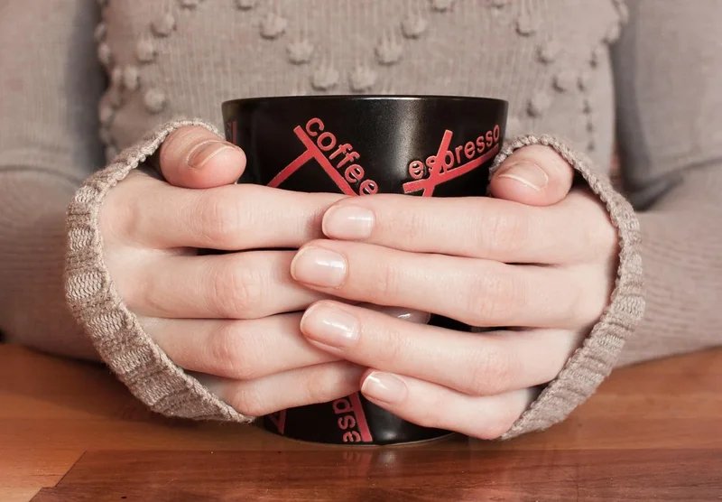 Mani che tengono una tazza di caffè nero in un ambiente accogliente, simbolo della cultura dei caffè di Kallio a Helsinki.