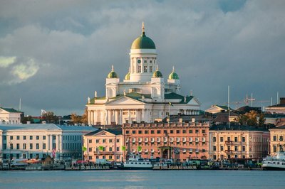 View of Helsinki Cathedral with historic buildings and the harbor in the foreground under a cloudy sky.
