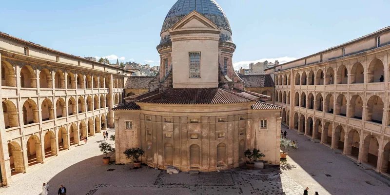 Vista del cortile e della cupola di un edificio storico nel quartiere Le Panier di Marsiglia, con archi e cielo sereno.