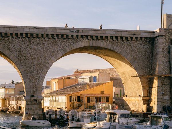 Vallon des Auffes a Marsiglia con ponte in pietra, barche nel porto e case colorate al tramonto.