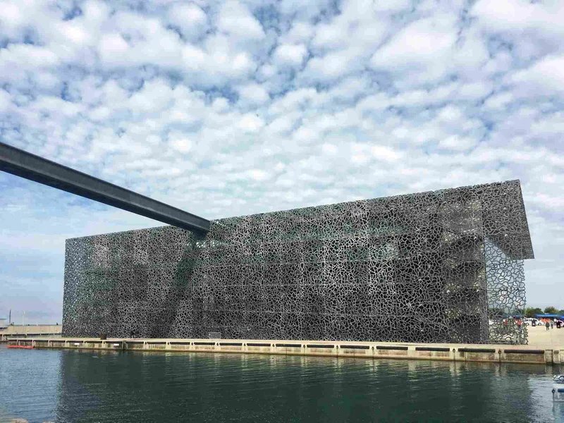 Vista del MuCEM a Marsiglia con cielo nuvoloso e riflessi sull'acqua.