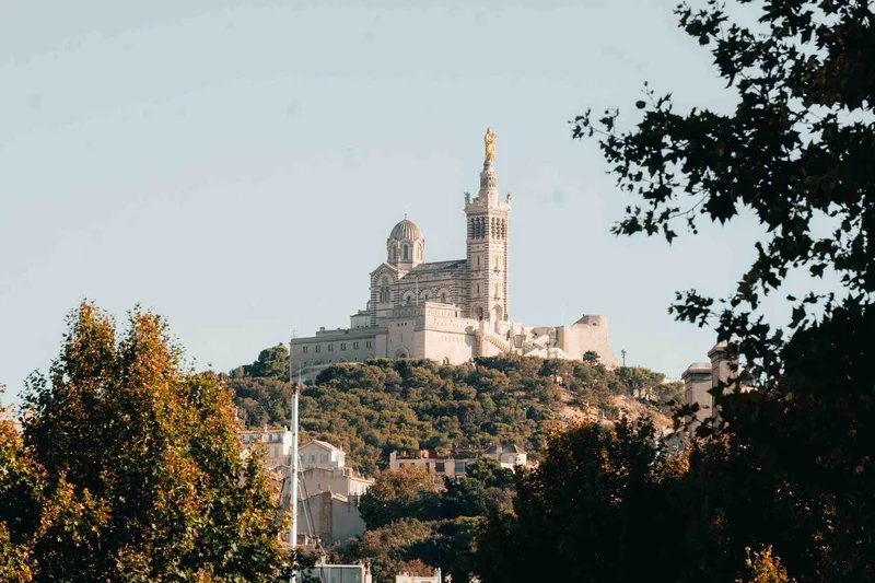 Basilica di Notre-Dame de la Garde a Marsiglia, vista panoramica con alberi in primo piano.