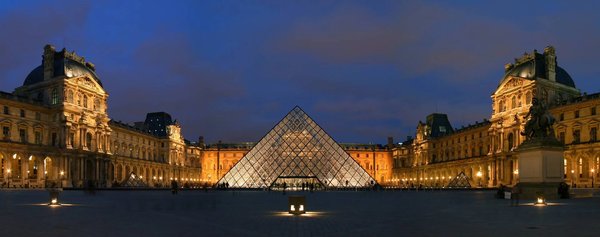 Night view of the illuminated glass pyramid of the Louvre Museum, with surrounding historic architecture in Paris.