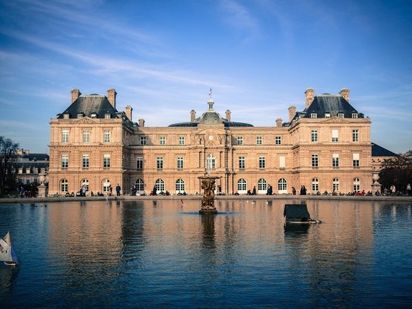 Luxembourg Palace and reflecting pool in the Luxembourg Gardens, Paris, with blue sky and architectural details.