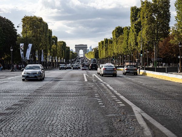 View of the Champs-Élysées with the Arc de Triomphe in the background, trees, and traffic on a cobblestone road in Paris.