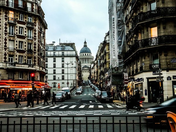 Street in Paris's Latin Quarter with the Panthéon in the background and lit cafés on the sides.