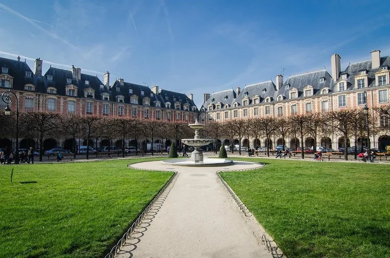 View of Place des Vosges in Le Marais, Paris, featuring a central fountain and historic buildings in the background.