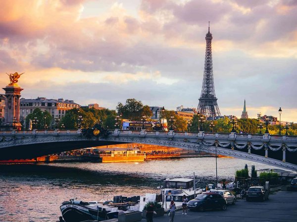 View of the Eiffel Tower at sunset with the Seine River and a Parisian bridge in the foreground.