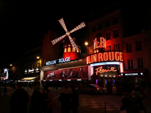 Illuminated facade of the Moulin Rouge in Paris with the iconic red windmill and neon signs at night.