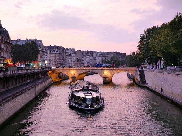 Evening cruise on the Seine in Paris with a view of an illuminated bridge and Parisian architecture at sunset.