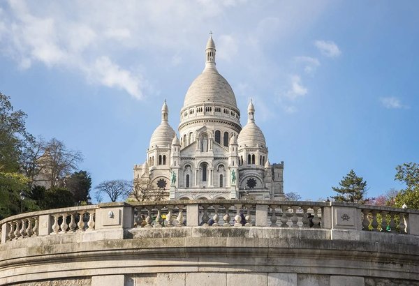 Sacré-Cœur Basilica in Montmartre, Paris, viewed from below with a blue sky and architectural details.