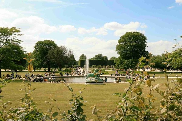 Luxembourg Gardens in Paris with a fountain, statues, and people picnicking on a sunny day.