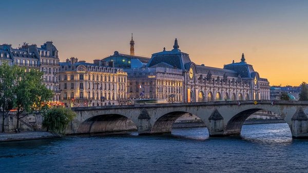 Evening view of the Orsay Museum and the Eiffel Tower in Paris, with a bridge over the Seine River.
