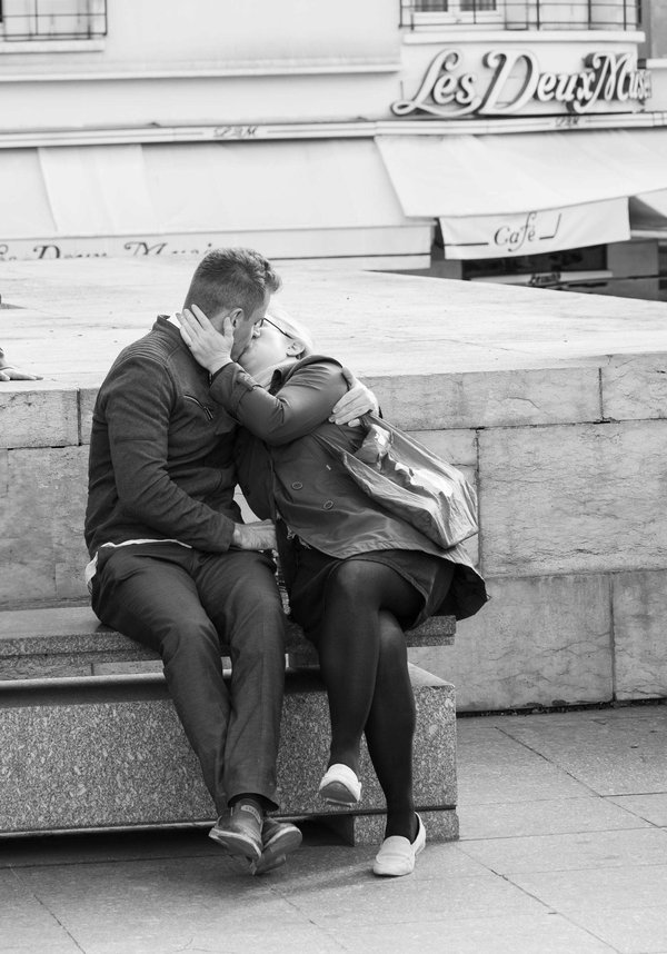 Romantic couple embracing in front of Les Deux Magots café in Paris, in black and white.