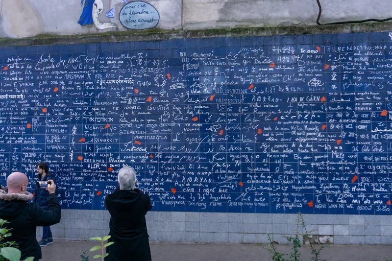 The Wall of Love in Paris with 'I love you' written in various languages, visitors taking photos.