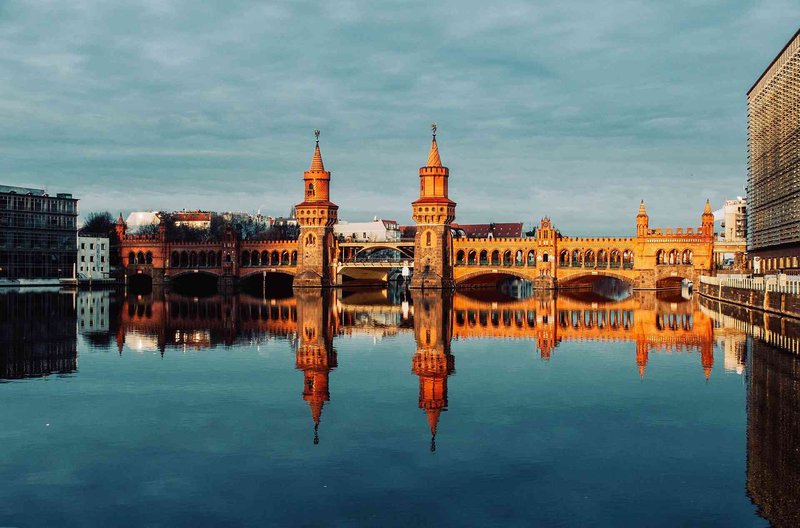 Oberbaum Bridge in Berlin with reflections on the water at sunset, an iconic city landmark.