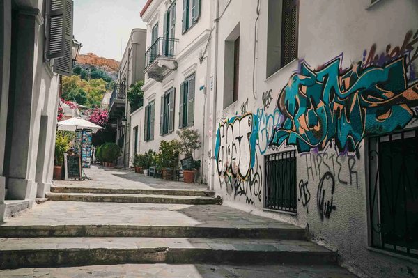 Narrow street in the Plaka neighborhood of Athens with traditional buildings, colorful graffiti, and potted flowers.